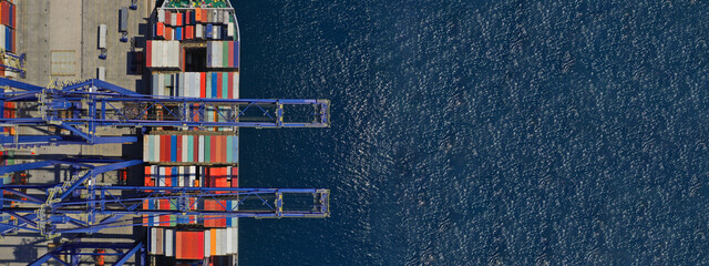 Aerial top down ultra wide photo of industrial container ship loading  - unloading colourful truck size containers with cranes in logistics terminal port