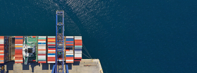 Aerial top down ultra wide photo of industrial container ship loading  - unloading colourful truck size containers with cranes in logistics terminal port