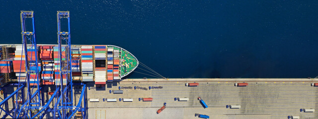 Aerial top down ultra wide photo of industrial container ship loading  - unloading colourful truck size containers with cranes in logistics terminal port - obrazy, fototapety, plakaty