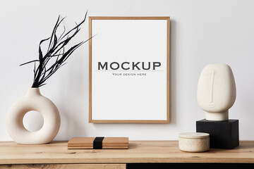 Stylish interior of living room with mock up poster frame, wooden commode, book, black leaf in ceramic vase and elegant personal accessories. Minimalist concept of home decor. Template. © FollowTheFlow