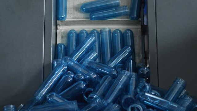 The blue preform from the hopper goes up the conveyor to the blowing machine. Production of plastic bottles at the mineral water bottling plant