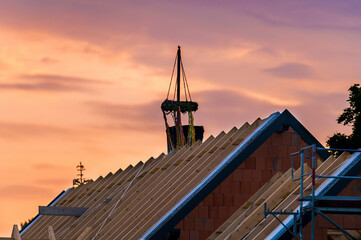 Ein Dachstuhl eines Neubaus mit Richtkranz bei Sonnenuntergang