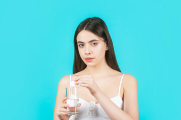 Girl take some pills, holds glass of water, isolated on blue. Young woman taking pill against...