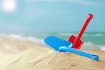 Red and blue plastic toy shovels on sandy beach near sea, space for text