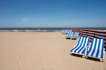 Blue-white sun beds on yellow sandy beach in small Belgian town De Haan or Le Coq sur mer, luxury...