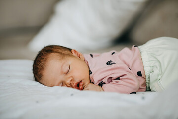 Newborn baby sleeping on bed on white blanket.