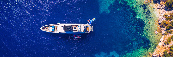Aerial view of anchored sailing yacht in emerald sea. Aerial view of a boat. Outdoor water sports, yachting. Aerial view of anchoring yacht in open water. Ocean and sea travel and transportation