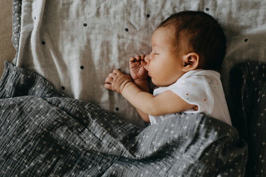 Newborn baby sleeping on her side, covered with a grey blanket.