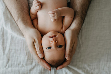 Portrait of a newborn baby with blue eyes, held by her father.