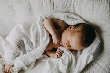 Fototapeten Newborn baby sleeping in a baby nest, covered with white muslin blanket. © Bostan Natalia