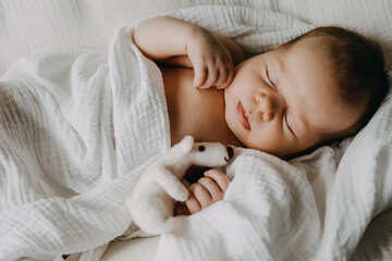 Newborn baby sleeping hugging a white bear toy.