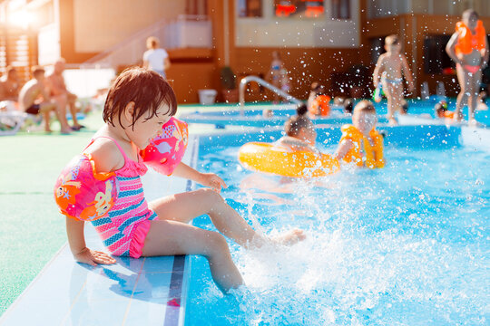 Little girl playing in outdoor swimming pool. Child inflatable armbands learning to swim in outdoor pool of resort.
