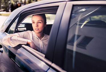 Serious woman in car. Sad, upset or tired taxi passenger. Cool elegant business lady sitting on the back seat looking out the window. Commuter late, waiting in traffic. Thoughtful female cab customer.