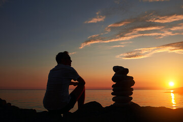 Silhouette of a man and zen stones on a ocean sea cliff in sunset sunrise time.