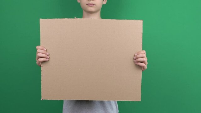 Boy holding in his hands blank empty cardboard poster on green chromakey screen background