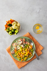Colorful pasta with boiled sausages in sour cream sauce, fresh vegetables and boiled cauliflower, water with kumquats
