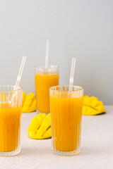 Freshly squeezed mango juice in glasses with a straw, ripe cut mango on a gray background