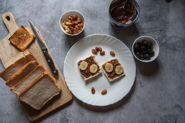 Top view of healthy breakfast food ingredients bread, peanut butter, bananas, almonds, nuts, dry fruits milk. Concept of wholesome and healthy food.
