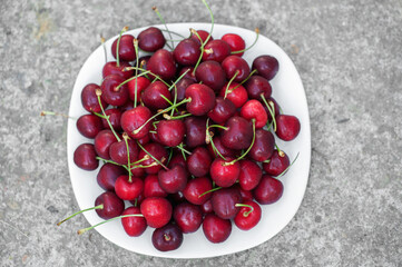 Ripe red cherries on a white plate on a neutral wooden background.