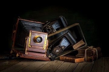 Cámaras fotográficas de fuelle vintage apiladas sobre una caja de madera y libros antiguos sobre...