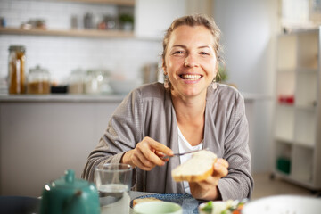 Beautiful woman enjoying in breakfast. Happy young woman eating sandwich at home..