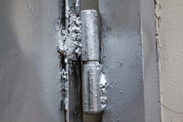 Low-quality welds on the hinges of the entrance iron gate painted with silver paint, close-up