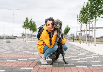 Smiling young woman in yellow hoodie hugging her fluffy shaggy gray dog, pet love and walking dog