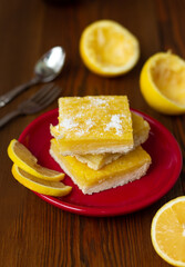 top view of juicy yellow lemon cakes on wooden background, stack of icing citrus cookies with lemon filling lying one on top of another on red plate