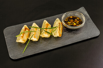 Japanese dumplings, gyozas, stuffed with steamed meat accompanied by a soy bowl with vegetables on a gray plate