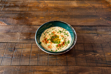 Fantastic Arabic chickpea hummus with olive oil, chopped parsley and paprika powder on the dark wooden table.