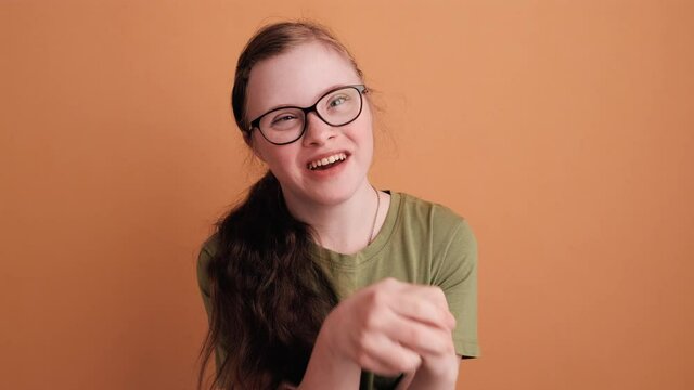 A smiling young girl with down syndrome is sitting and talking about something isolated over orange wall in the studio