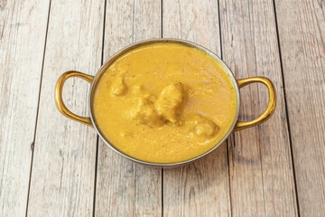 Bowl with mild chicken korma yellow curry with yogurt sauce and coconut milk on white table