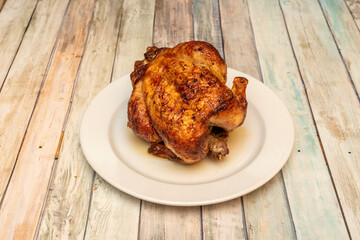 Whole chicken roasted in a rotisserie with very crispy skin on white plate and wooden table