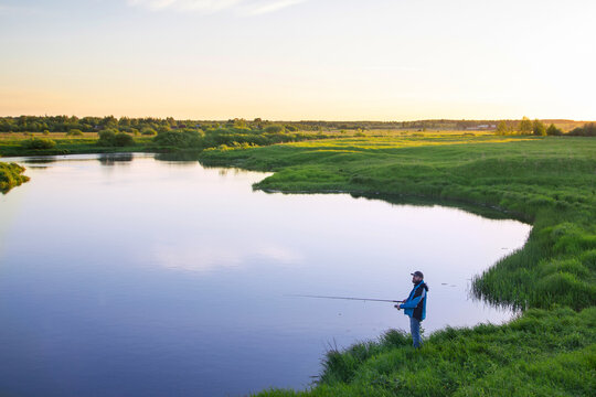 river bank on a summer evening, a man in a jacket with a fishing rod catches fish