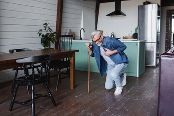 Sick man with crutch holding hand on chest while falling on floor