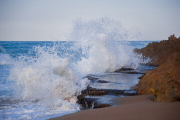 powerfull tide waves crash harsh strong on terracotta rocks at sunset dask on Caribbean island on the coast of the Atlantic Ocean