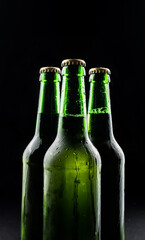 Three bottles of beer from green glass on black background.