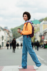 Obraz premium African american woman with coffee to go and smartphone walking on urban street