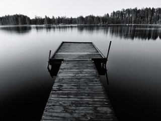 Black and white photo of a jetty at sunset on the Swedish lakes surrounded by forest