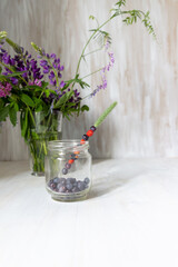 Fresh blackberry and strawberry beaded on grass in jar with berries and forest flowers in a glass vase on white background