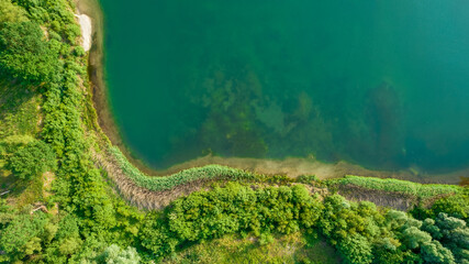 Aerial view of a picturesque place where transparent turquoise water of a forest lake meets a stony shore with trees in spring. captured with a drone. High quality photo