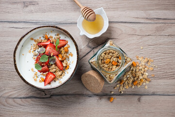 Bowl of yogurt served with granola, fresh strawberry and honey, above view on a brown wooden background, horizontal shot