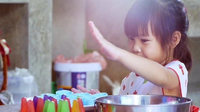 Cute siblings girls are scooping small pieces of Pipo jelly in different colors in a mold to prepare for dessert. Children make jelly desserts in the kitchen at home together.