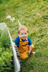 Kid sitting on the grass next to a garden cart and smiling