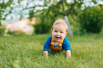 A baby boy lies on the grass in the garden and laughs