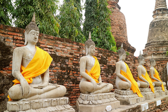 Row of the Amazing Buddha Images in Yellow Robes with Group of Stupas in Backdrop, Wat Yai Chai Mongkhon Temple, Ayutthaya, Thailand	