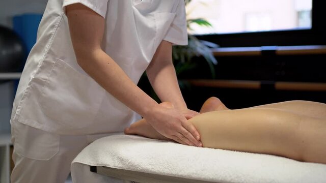 Anonymous female physiotherapist massaging leg of crop woman