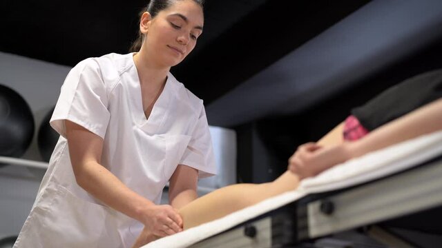 Smiling female physiotherapist massaging leg of crop woman