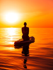 Young woman on stand up paddle board at quiet sea with bright sunset or sunrise. Woman on sup board and sunset with reflection