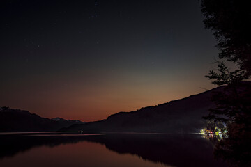 Quiet lake at late night in Los Alerces National Park. Lights can be seen from a base camp.